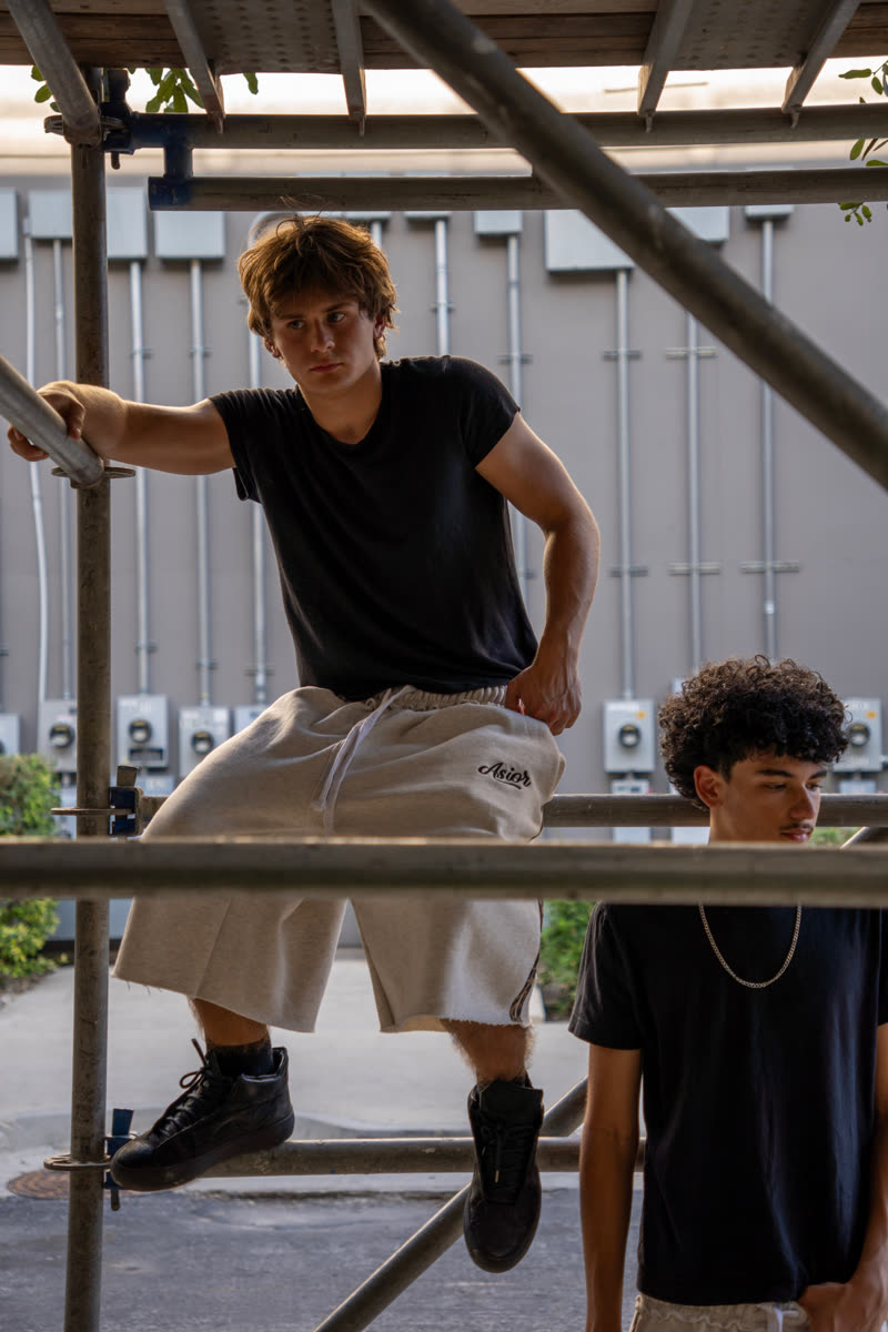 Two models under a scaffold, one in light Asior shorts