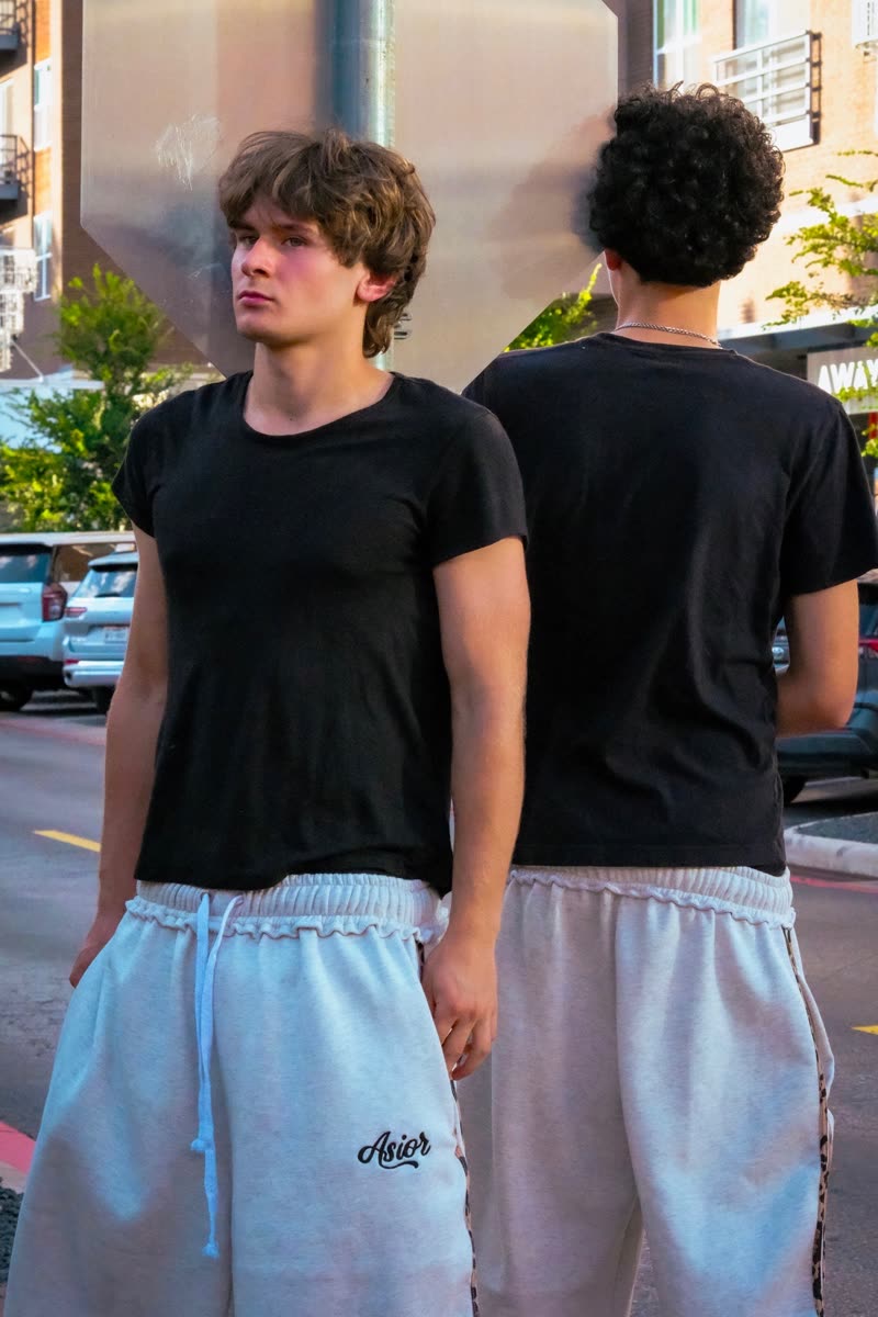 Two models in black tees and light shorts beside a parked car