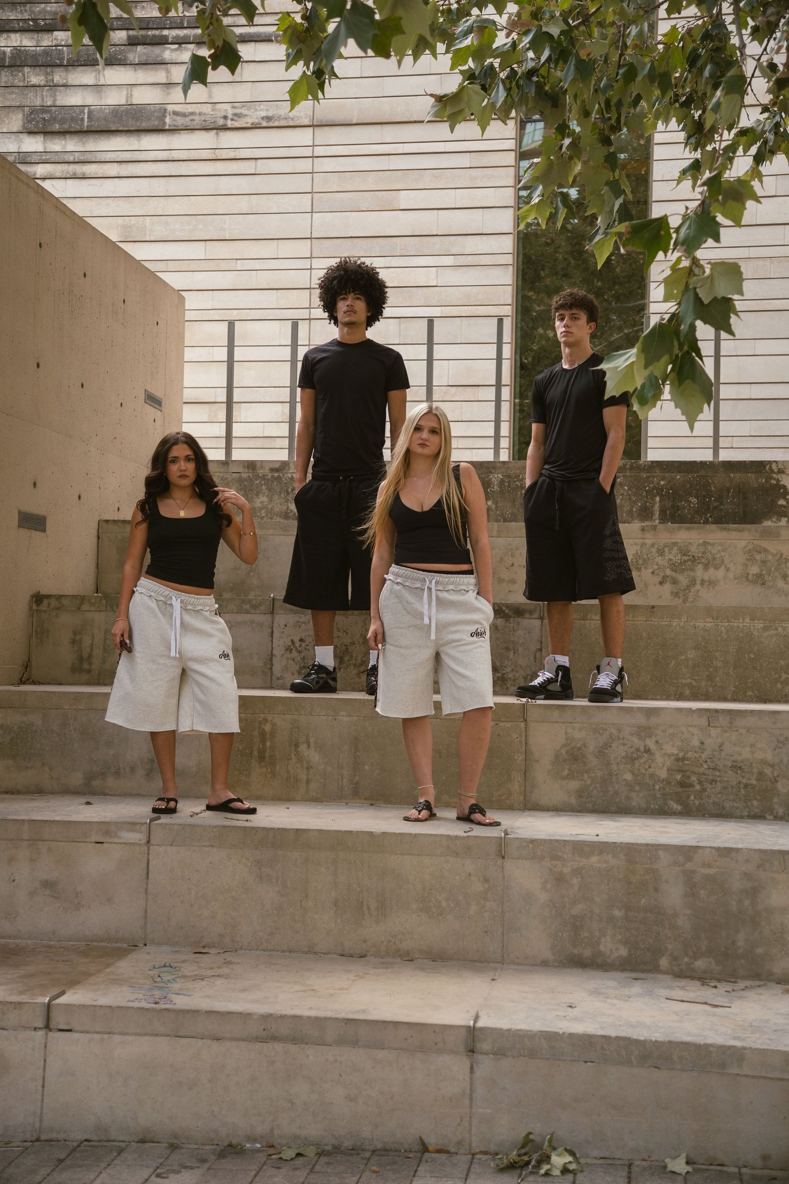 Four models in Asior tees, tanks and sweat shorts on concrete steps