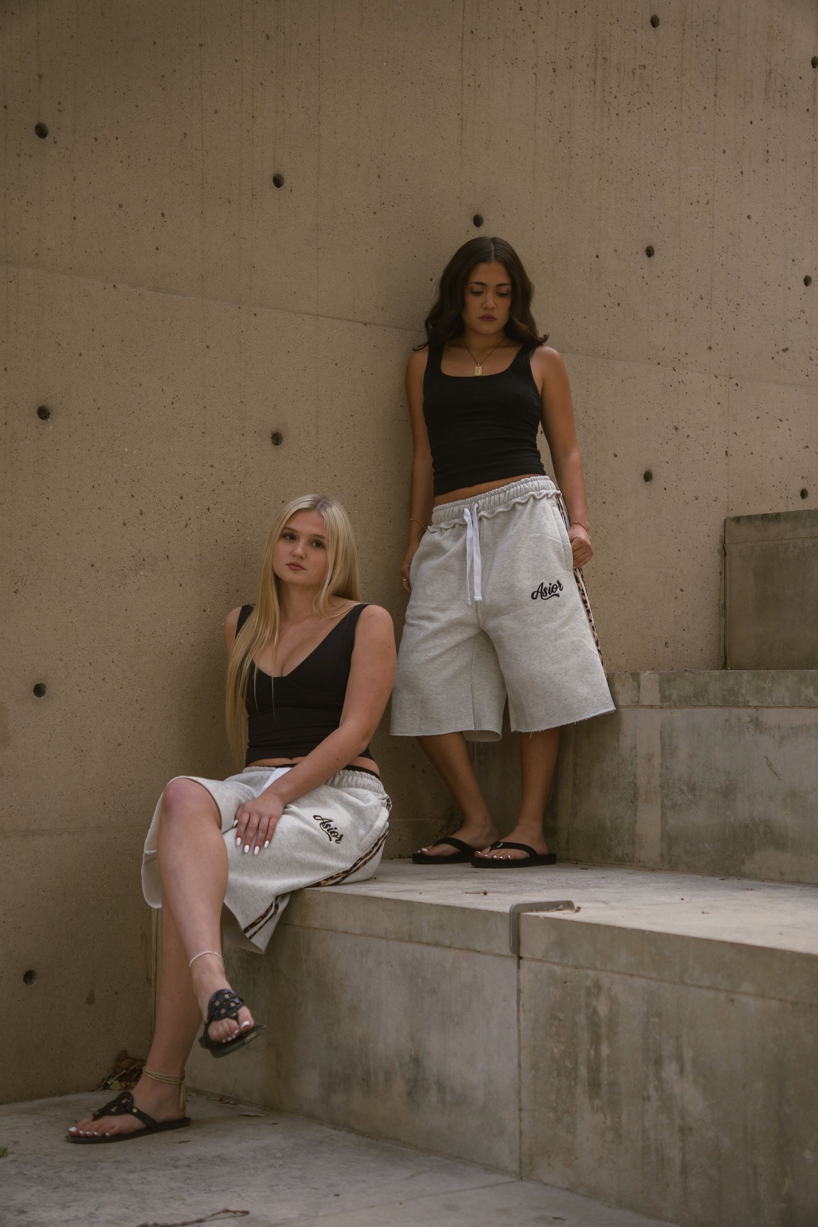 Two models in Asior sweat shorts on concrete steps