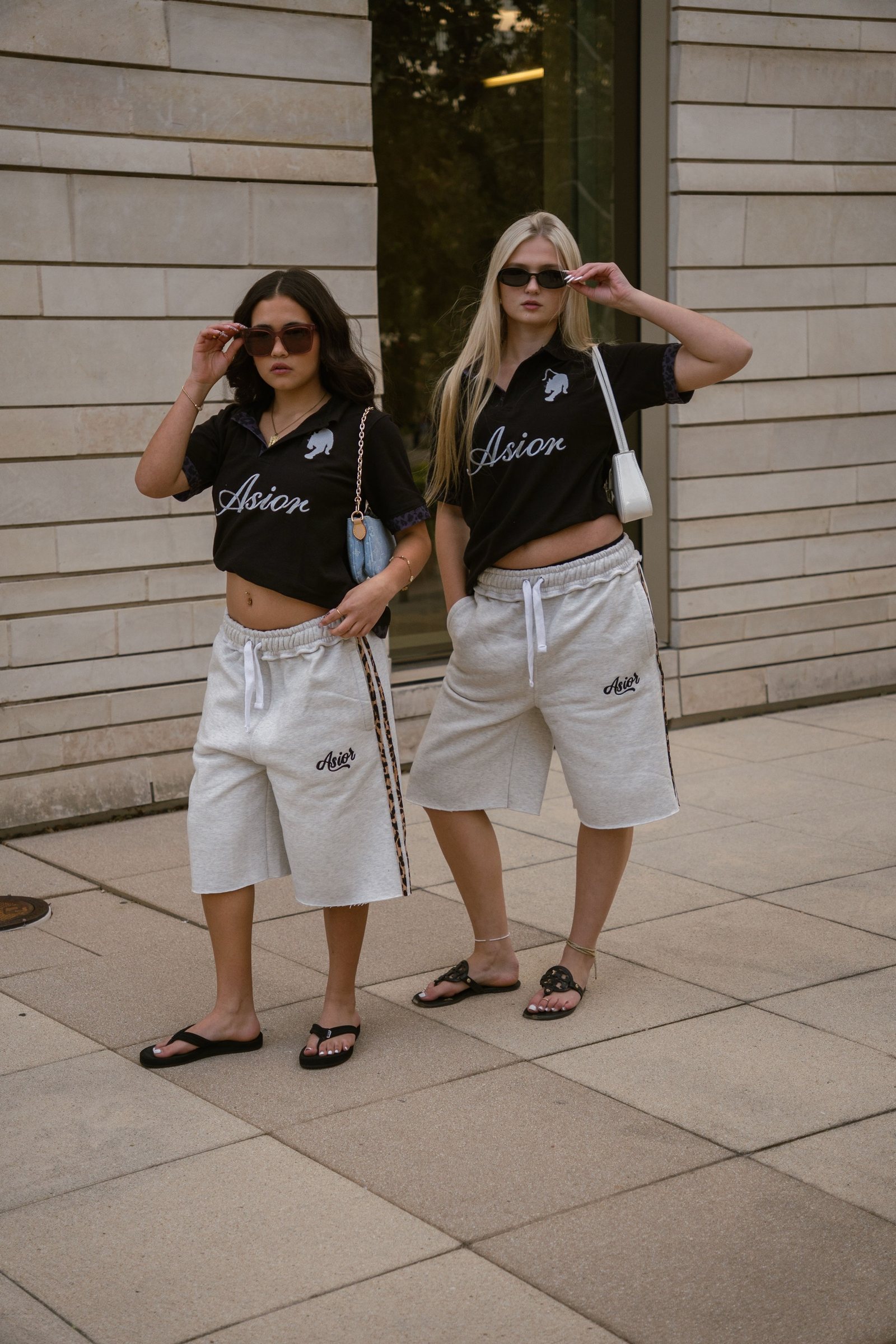 Two models in Asior polos and sweat shorts against a stone wall
